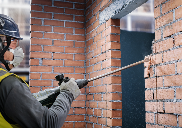 PRO SDS max-4C 플랫 치즐, 25 x 600mm 안전 장비를 착용한 사람이 철거 망치로 벽돌 벽을 깎고 있습니다.