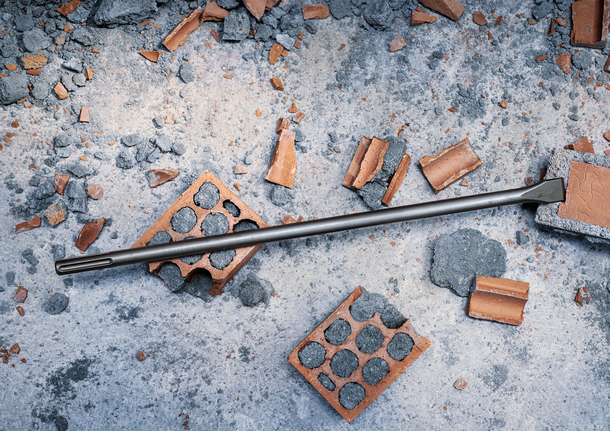 PRO SDS max-4C 플랫 치즐, 25 x 600mm 깨진 벽돌과 콘크리트 잔해 위에 끌 비트가 놓여 있습니다.