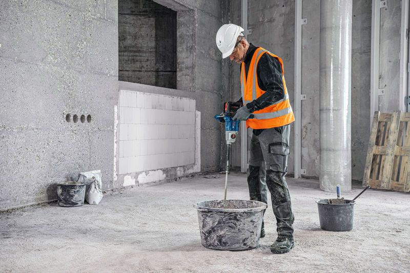 안전 장비를 착용한 사람이 건설 현장에서 교반 장치를 이용해 재료를 섞고 있습니다.