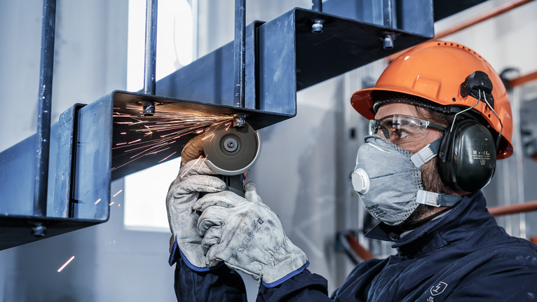 안전 장비를 착용한 사람이 분쇄기로 금속 계단을 자릅니다.