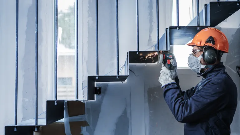 안전 장비를 착용한 사람이 금속 계단을 갈아서 불꽃이 튀는 모습.