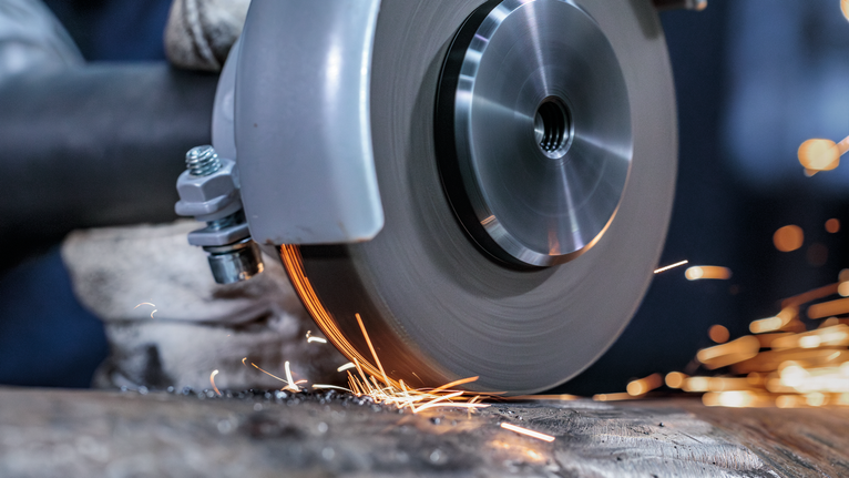 안전 장비를 착용한 사람이 전동 공구로 금속을 갈아서 불꽃을 낸다.