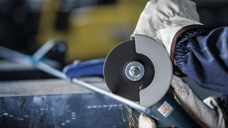 안전장비를 착용한 사람이 각도 그라인더를 사용하여 금속 파이프를 자릅니다.