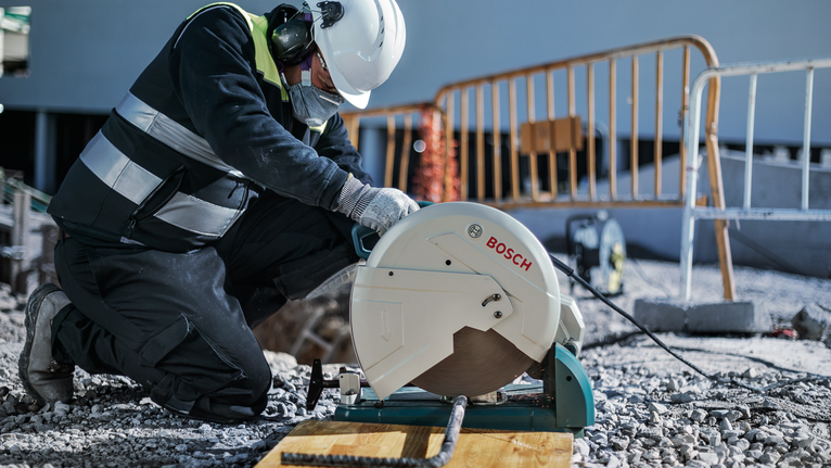 안전 장비를 착용한 작업자가 건설 현장에서 절단톱을 이용해 철근을 자릅니다.
