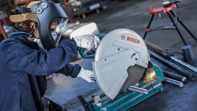 안전 장비를 착용한 사람이 원형 톱으로 금속 파이프를 자르는데, 불꽃이 튀네요.