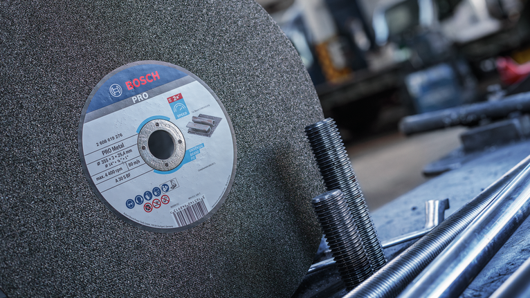 작업장에서 나사산이 있는 금속 막대 옆에 대형 연마 절단 디스크를 배치한 모습입니다.