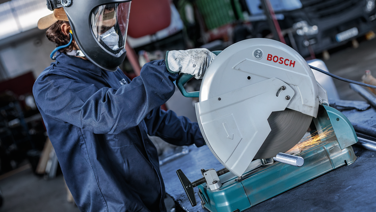 안전 장비를 착용한 사람이 원형 톱으로 금속 파이프를 절단하고 있습니다.