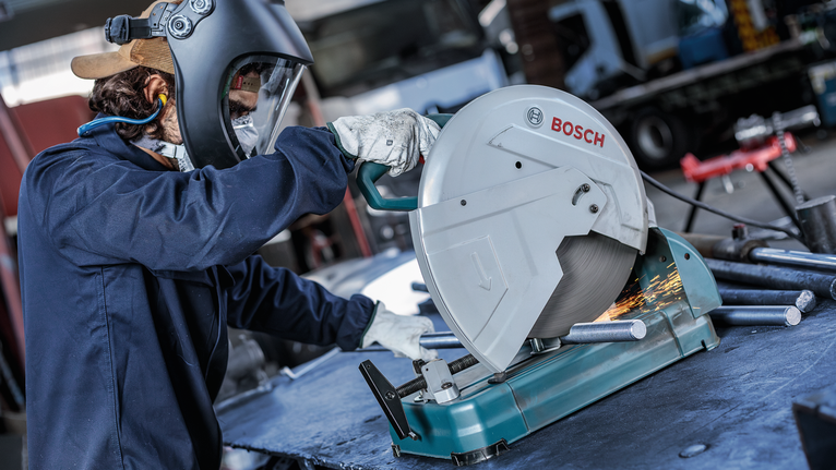 안전 장비를 착용한 사람이 전기톱으로 금속 파이프를 자르면서 불꽃이 튀는 모습입니다.