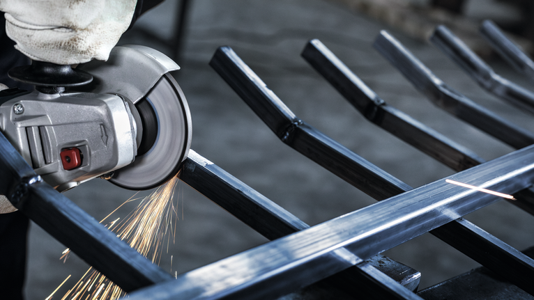 안전 장비를 착용한 사람이 각도 분쇄기를 사용해 금속을 절단하면서 불꽃을 일으킵니다.