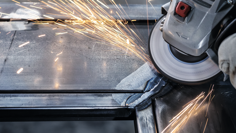 안전장비를 착용한 사람이 금속을 갈아서 밝은 불꽃을 낸다.