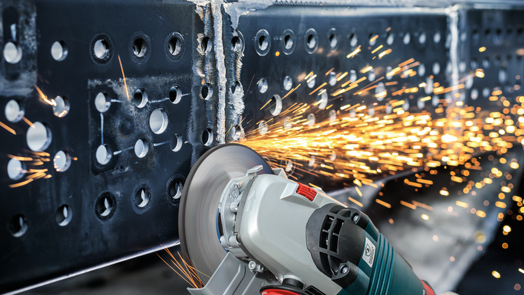 불꽃이 튀는 가운데 각도 분쇄기가 금속 빔을 절단합니다.