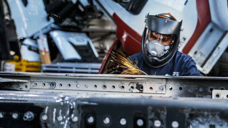 안전장비를 착용한 사람이 금속을 갈아서 밝은 불꽃을 일으킨다.