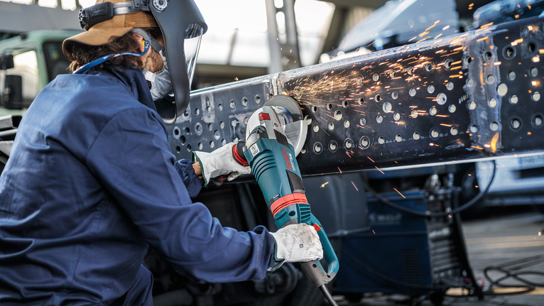 안전 장비를 착용한 사람이 금속 빔을 갈아서 밝은 불꽃을 발생시킨다.