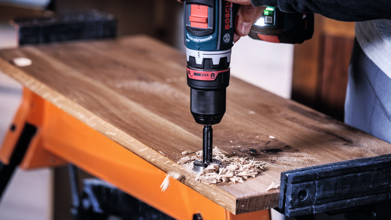 나무 판자에 구멍을 뚫기 위해 전동 드릴을 사용하는 사람.