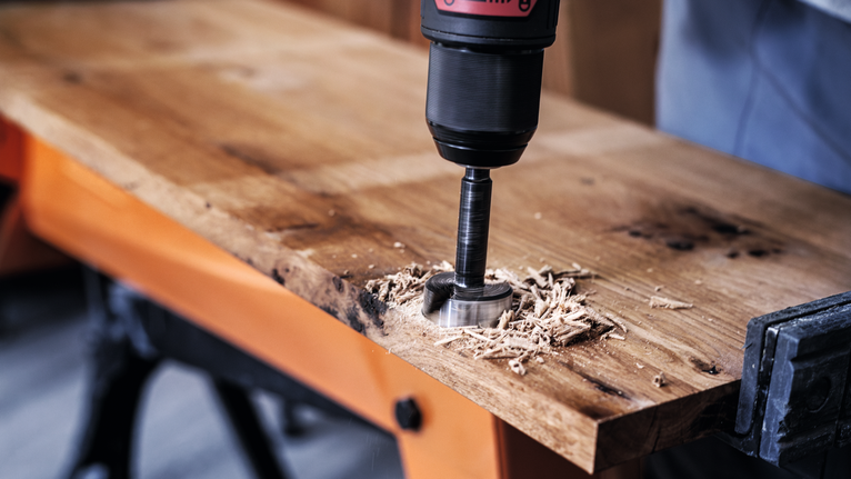 한 사람이 홀 톱 비트가 달린 전동 드릴을 사용하여 나무 판자를 자릅니다.