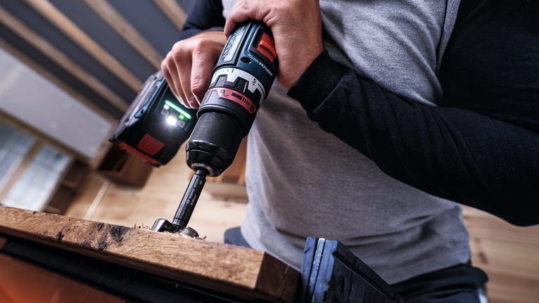 사람이 무선 드릴을 사용해 나무판에 나사를 박고 있습니다.