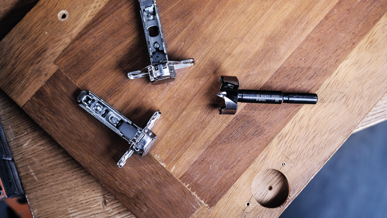 새로 뚫은 구멍이 있는 나무 패널에 드릴 비트와 경첩을 올려놓았습니다.