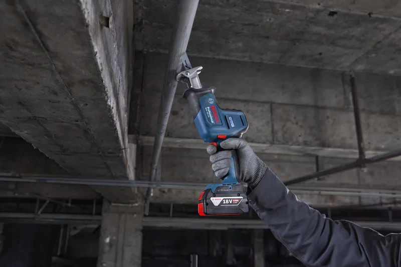 안전 장비를 착용한 사람이 왕복톱을 이용해 머리 위의 금속 파이프를 자릅니다.