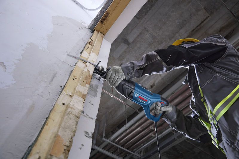 안전장비를 착용한 사람이 왕복톱을 사용해 벽을 자르고 있습니다.