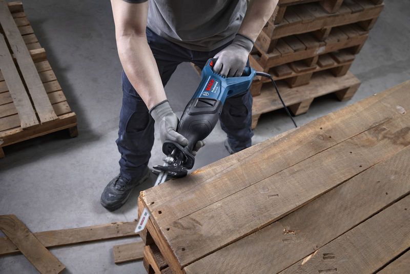 안전 장비를 착용한 사람이 왕복톱을 사용해 나무 팔레트를 자릅니다.