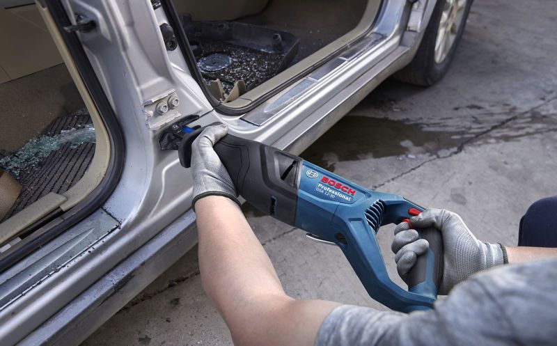 안전 장비를 착용한 사람이 왕복톱을 사용해 자동차 문틀의 금속을 자르고 있습니다.