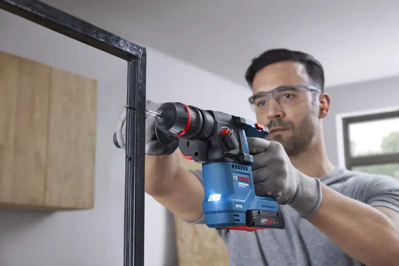 안전장비를 착용한 사람이 무선 회전 망치를 이용해 금속 프레임에 구멍을 뚫고 있습니다.