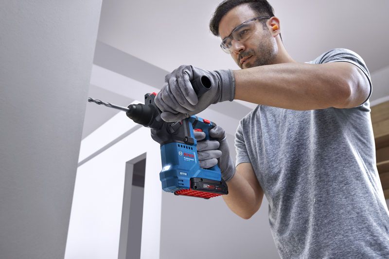 안전장비를 착용한 사람이 회전 망치로 벽에 구멍을 뚫고 있습니다.