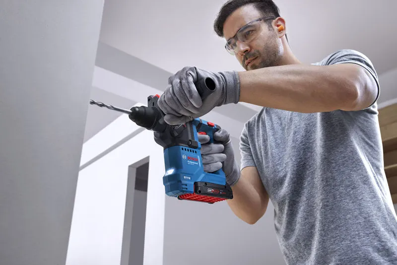 안전장비를 착용한 사람이 회전 망치로 벽에 구멍을 뚫고 있습니다.