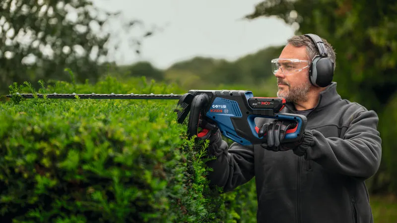 GHE 18V-50 (II) 안전장비를 착용한 사람이 전기 울타리 트리머로 울타리를 다듬고 있습니다.