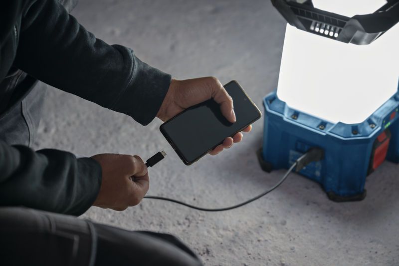 콘크리트 바닥에서 무선 작업 현장 조명을 이용해 스마트폰을 충전하는 사람.