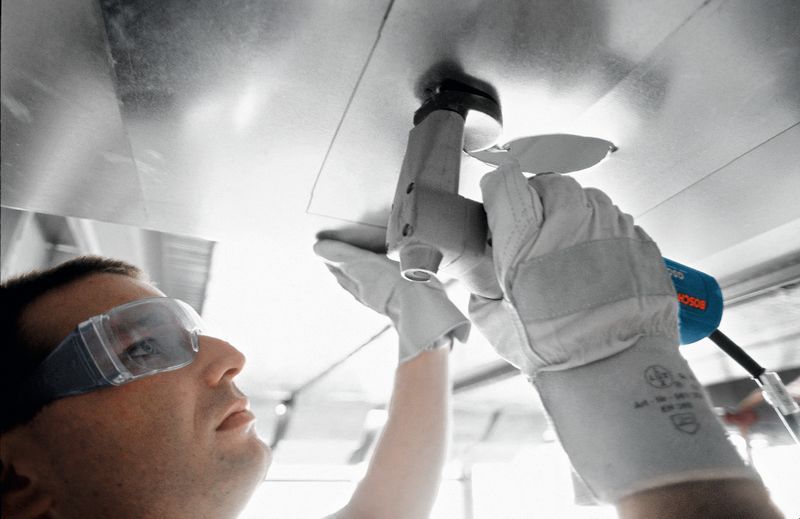 안전 장비를 착용한 사람이 가위를 사용하여 금속판을 자릅니다.