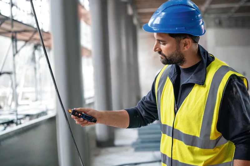 안전 장비를 착용한 사람이 비접촉 전압 테스터로 케이블을 테스트하고 있습니다.