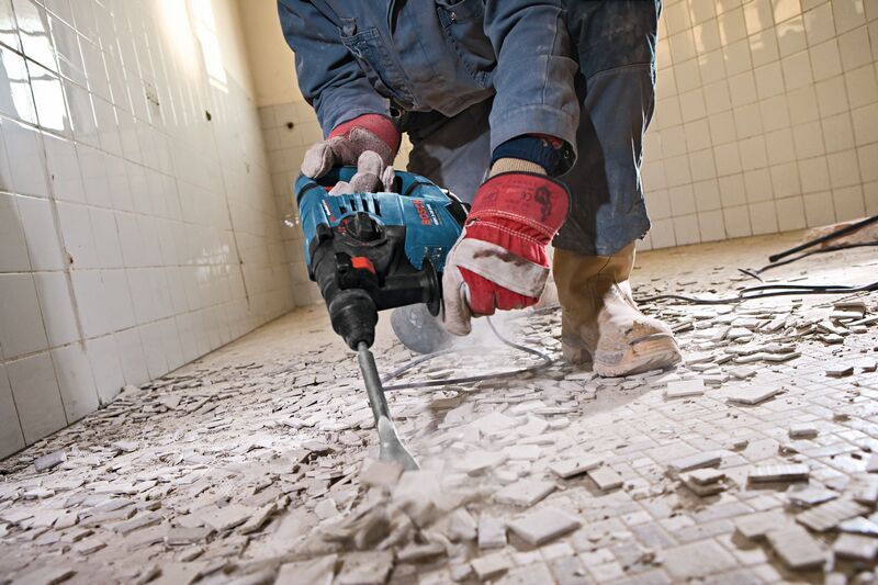 안전장비를 착용한 사람이 파괴망치를 사용해 바닥 타일을 제거하고 있습니다.