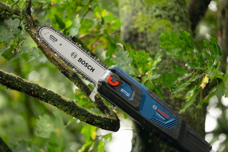 잎이 무성한 야외에서 무선 망원 가지치기 가위로 나무 가지를 자르고 있습니다.