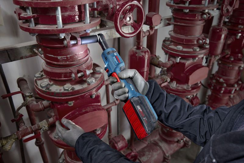 안전장비를 착용한 사람이 무선 래칫 렌치로 파이프 볼트를 조이고 있습니다.