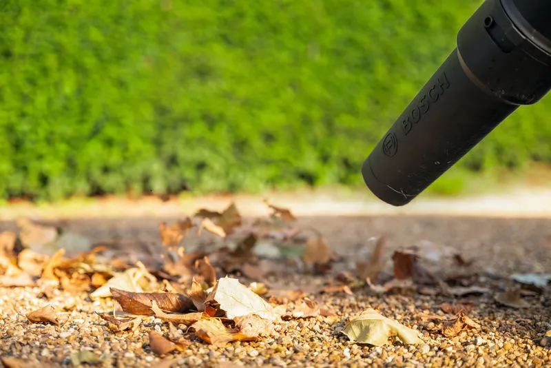 전동 송풍기 노즐을 이용해 야외 자갈길을 따라 마른 잎을 옮깁니다.