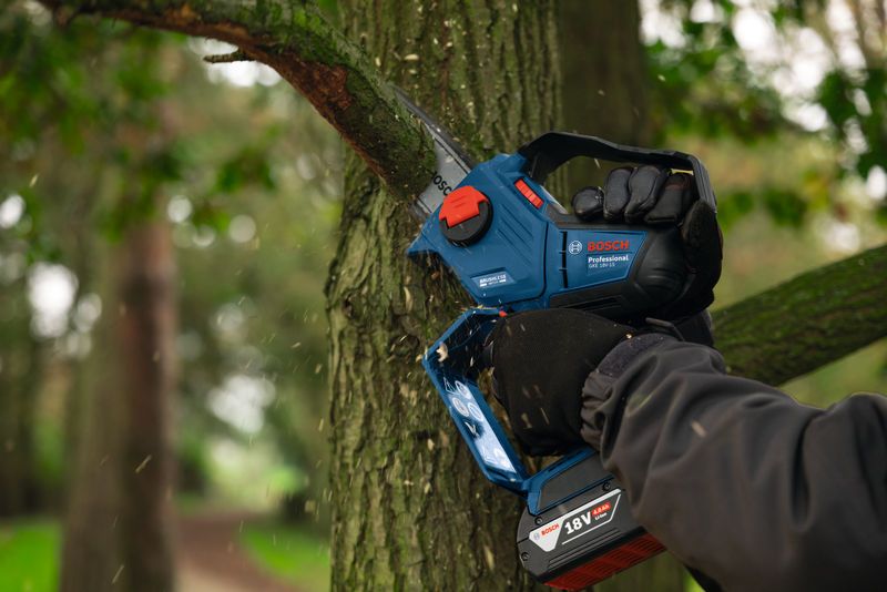 안전장비를 착용한 사람이 무선 가지치기 톱을 사용하여 나무가지를 다듬고 있습니다.