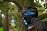 안전장비를 착용한 사람이 무선 가지치기 톱을 사용하여 나무가지를 다듬고 있습니다.
