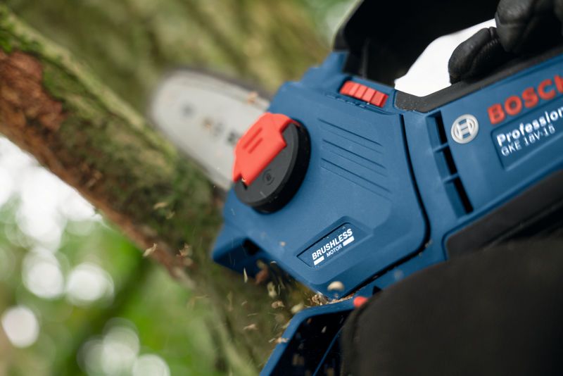 안전 장비를 착용한 사람이 파란색 전기톱을 사용하여 나무가지를 자르고 있습니다.