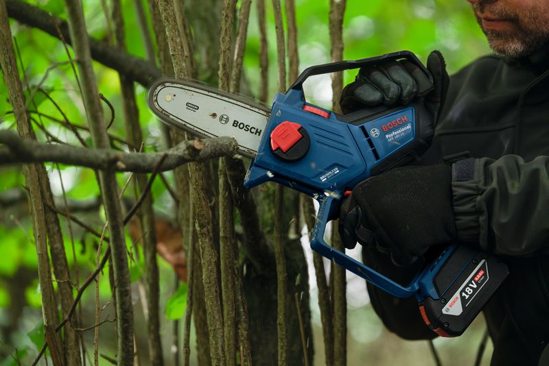 안전장비를 착용한 사람이 무선 가지치기 톱을 사용하여 나무 가지를 다듬고 있습니다.