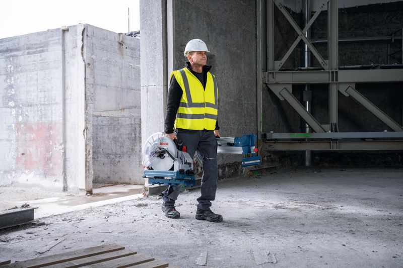 안전 장비를 착용한 사람이 미완성 건물에서 금속 절단 톱을 들고 있습니다.