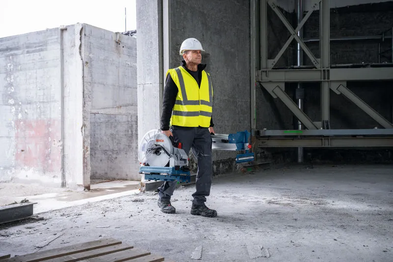 안전 장비를 착용한 사람이 미완성 건물에서 금속 절단 톱을 들고 있습니다.