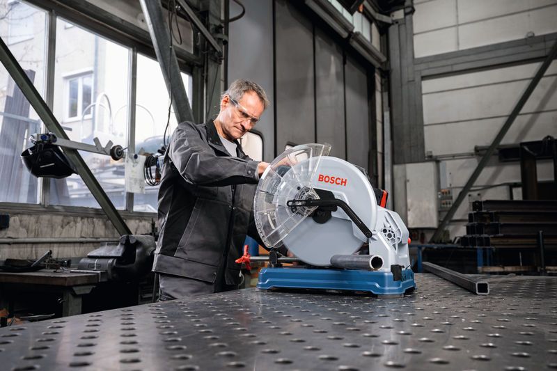 안전 장비를 착용한 사람이 작업장에서 금속 절단 톱을 조작하고 있습니다.