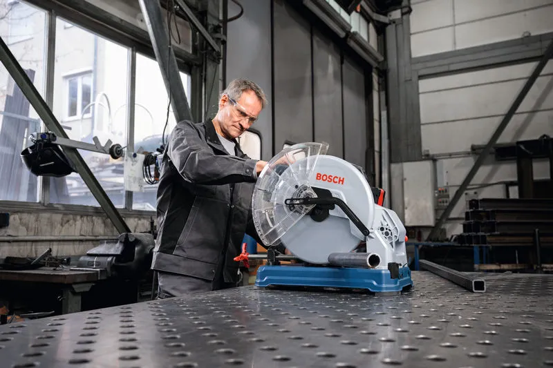 안전 장비를 착용한 사람이 작업장에서 금속 절단 톱을 조작하고 있습니다.