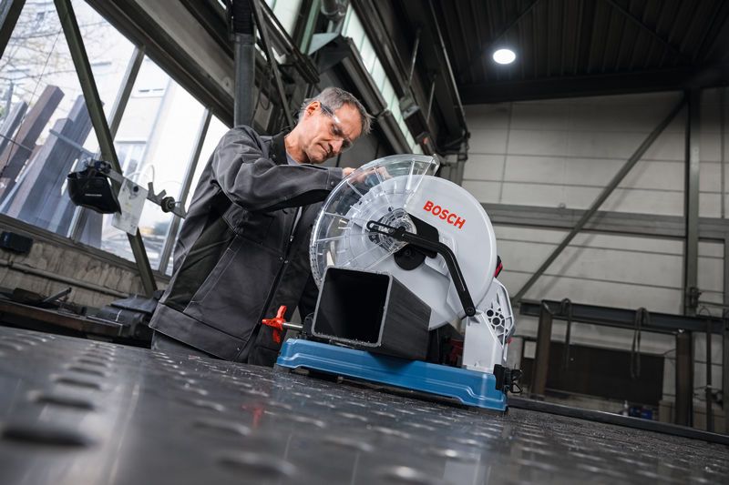 안전 장비를 착용한 사람이 금속 파이프를 절단하기 위해 금속 절단 톱을 준비하고 있습니다.