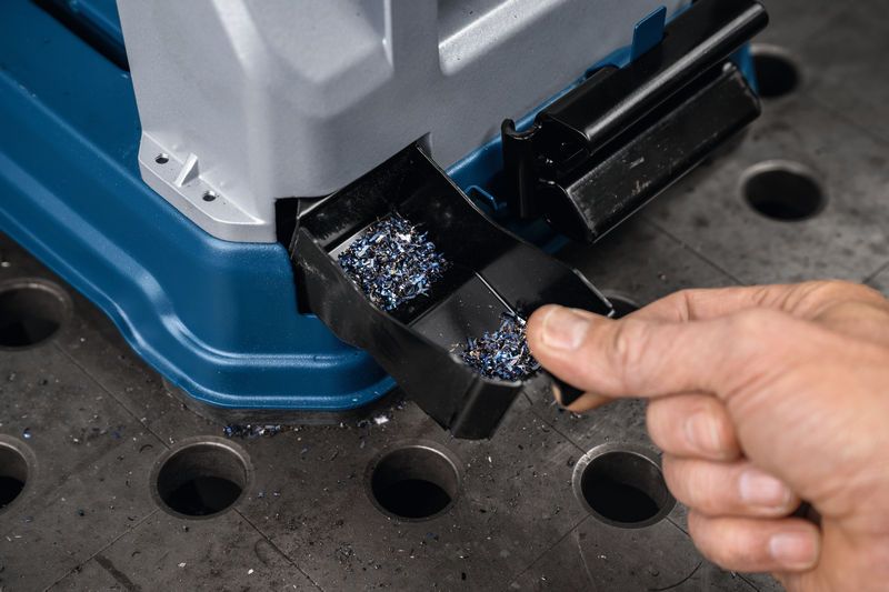 한 사람이 작업대 위의 금속 절단 톱에서 금속 칩 트레이를 비우고 있습니다.