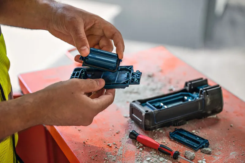 안전 장비를 착용한 사람이 먼지 쌓인 작업대에서 전동 공구의 배터리를 교체하고 있습니다.
