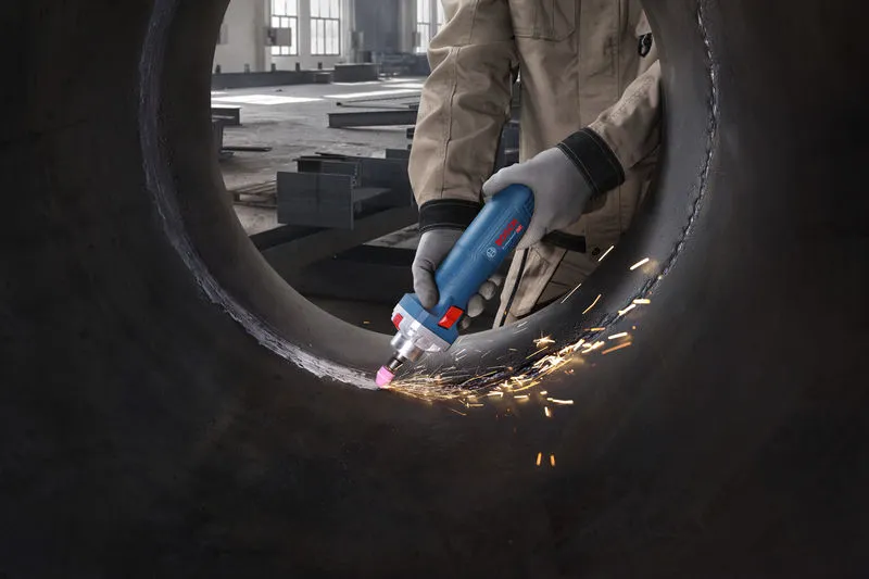 안전장비를 착용한 사람이 직선형 그라인더를 이용해 큰 금속 파이프의 내부를 갈고 있습니다.