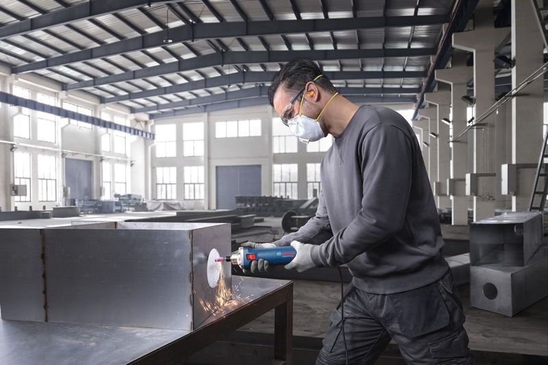 안전 장비를 착용한 사람이 직접 그라인더를 사용하여 금속 상자를 갈고 있습니다.