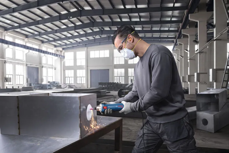 안전 장비를 착용한 사람이 직접 그라인더를 사용하여 금속 상자를 갈고 있습니다.